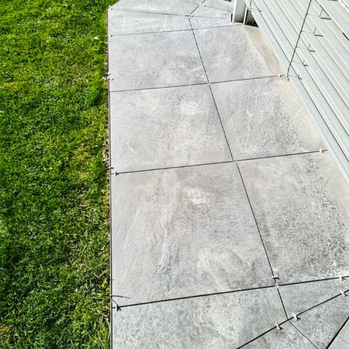 Terrasse extérieure avec dalles en béton gris disposées en carreaux réguliers, délimitée par une bordure nette séparant le dallage de la pelouse verte