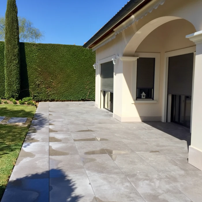 Terrasse extérieure résidentielle avec dallage en pierre naturelle beige, maison moderne à crépi blanc et arcades