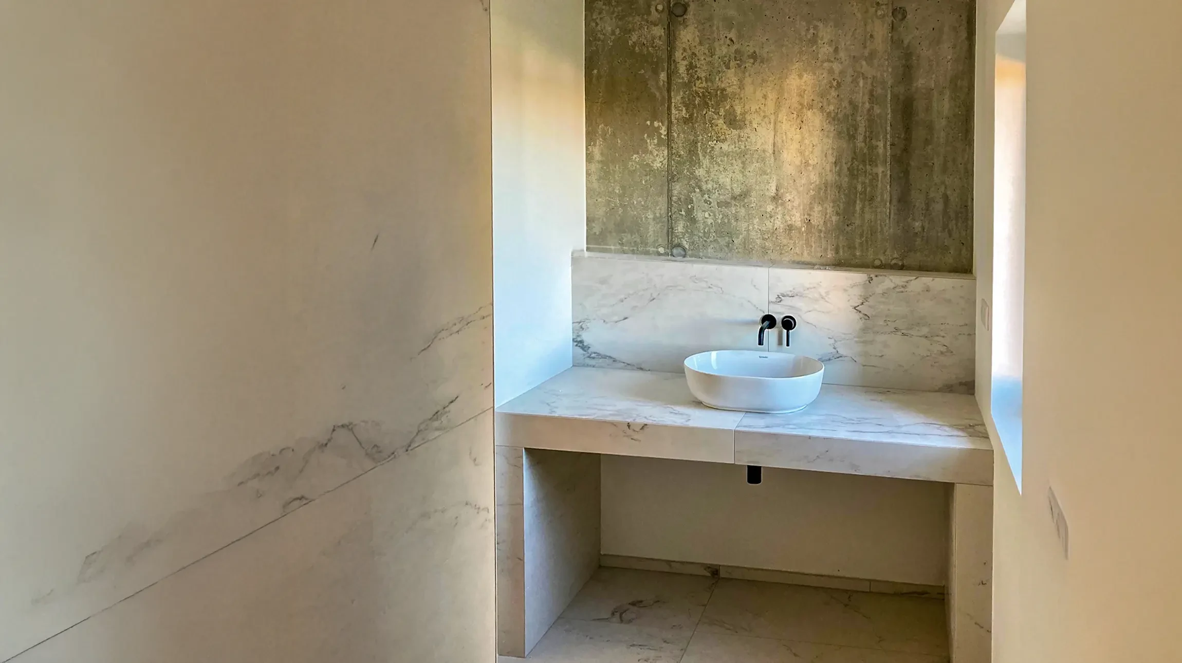 Salle de bain moderne avec douche à l'italienne vitrée, meuble vasque suspendu en bois clair, miroir rond et carrelage mural texturé vert-gris